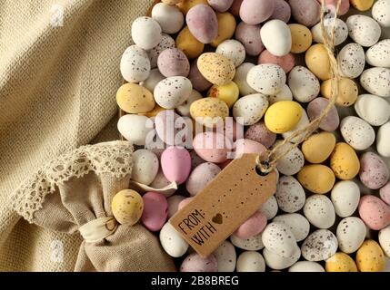 Mehrere farbenfrohe Ostereier aus Schokolade auf dem runden Teller, Geschenkbeutel aus Leinwand, Frühlings-Blumenstrauß. Flatlay, Ansicht nach oben. Ostern, Frühlingssymbol Stockfoto