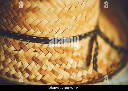 Ein Strohhut eines alten Bauern mit einem schwarzen Band, das in einem Bogen gebunden ist, wird im heißen Sommerlicht beleuchtet. Stockfoto