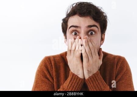 Nahaufnahme des Überraschungsporträts erschrocken junge gutaussehende Männer mit Borsten, staunend mit knallenden Augen, vergasend, den Mund mit Händen als seiend bedecken Stockfoto