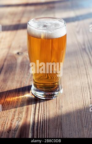 Glas kaltes Bier auf dem Holztisch einer Kneipe unter natürlichem Nachmittaglicht Stockfoto