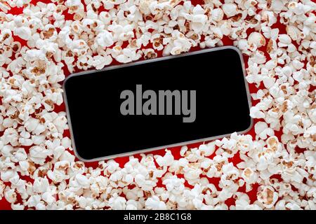 Smartphone in einem Haufen Popcorn mit leerem Bildschirm. Konzept zum Ansehen oder Streamen von Online-Filmen. Stockfoto