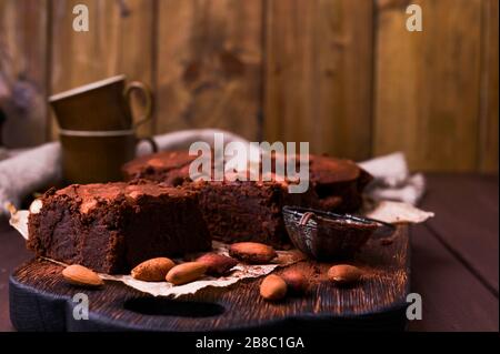 Brownie, Schokoladenkuchen mit Mandeln auf einem Holzbrett, mit Kakao bestreut. Serviert werden hausgemachte Kuchen. Draufsicht. Freier Speicherplatz für Text. Stockfoto