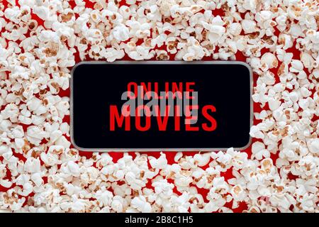 Smartphone in einem Haufen Popcorn mit Online-Filmen Wörter auf dem Bildschirm. Konzept zum Ansehen oder Streamen von Online-Filmen. Stockfoto