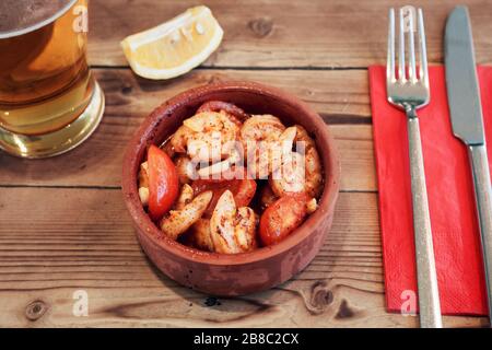 Garneleneintopf in einer Pfanne mit Tomaten, Gewürz und Bier, serviert auf einem Holztisch. Stockfoto