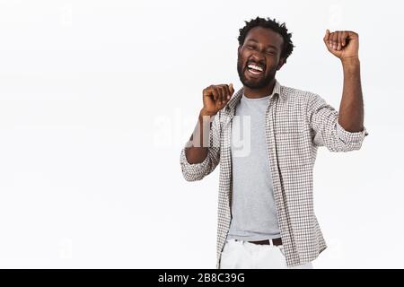 Glücklicher, begeisterter, gutaussehender afroamerikanischer bärtiger Mann tanzt glücklich, feiert Erfolg, hebt die Hände in die Höhe, erzielt Sieg oder Stockfoto