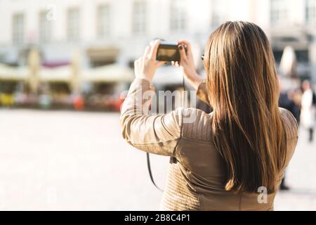 Tourist fotografieren auf dem Stadtplatz im Urlaub mit der Kamera. Frau, die in der Stadt ein Urlaubsbild gemacht hat. Tourismuskonzept. Rückansicht der weiblichen Person. Stockfoto