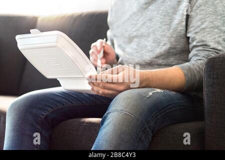 Mann, der fast Food von der Take-away-Box nach Hause auf der Couch isst. Abendessen vom chinesischen Restaurant oder vom Junk Food Restaurant. Kerl genießt Kebab oder Salat. Stockfoto