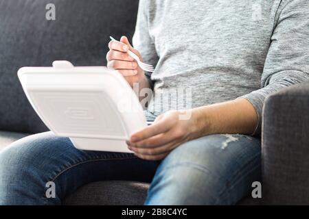 Kerl, der Essen wegnimmt. Mann, der Kebab oder chinesisch aus Fast-Food-Box genießt. Sie sitzen zu Hause auf der Couch und haben ein Essen zum Mitnehmen. Stockfoto