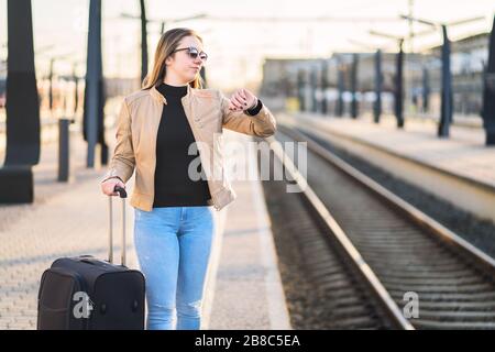 Unglückliche und frustrierte Frau, die die Zeit betrachtet und am Bahnhof zuschaut. Verärgerter Passagier auf Bahnsteig. Stockfoto