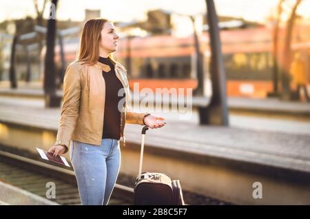 Frustrierte Frau am Bahnhof. Verspätet, verzögert, storniert oder hinter dem Zeitplan zurückgestellt. Unglücklicher und trauriger Passagier verlor auf falscher Plattform. Stockfoto