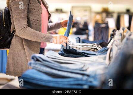 Frau kauft Jeans im Modegeschäft. Weibliche Kunden halten Hosen und schauen sich Stoff und Material an. Stockfoto