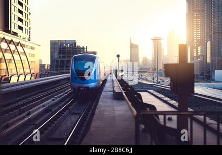 U-Bahn bei Sonnenuntergang in der modernen Stadt. U-Bahn Dubai. Skyline im Stadtzentrum mit Sonnenuntergang. Wolkenkratzergebäude und Autoverkehr auf der Autobahn. Stockfoto