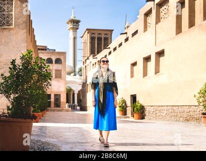 Frau, die im alten Dubai, VAE, spazieren geht. Traditionelle arabische Straße und Moschee. Weibliche Touristin im historischen Viertel Al Fahidi mit Kleid. Stockfoto