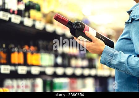 Alkoholregal im Spirituosenladen oder im Supermarkt. Frau kauft eine Flasche Rotwein und schaut im Geschäft auf alkoholische Getränke. Stockfoto