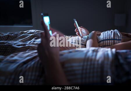 Gelangweilte Paare, die sich nachts im Bett liegend ignorieren, während sie Mobiltelefone verwenden. Smartphone-Süchtiger. Besessen und abgelenkt Mann und Frau. Stockfoto