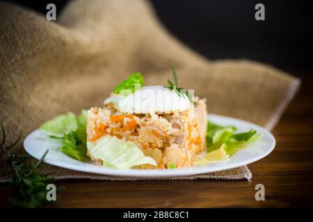 Gekochten Reis mit Gemüse und gebratenem Ei mit Salatblättern in einem Teller auf einem Holztisch Stockfoto