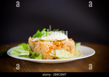 Gekochten Reis mit Gemüse und gebratenem Ei mit Salatblättern in einem Teller auf einem Holztisch Stockfoto