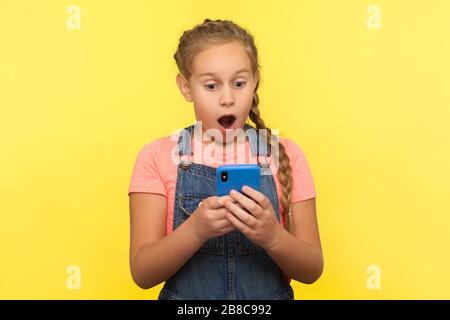 Porträt des schockierten kleinen Mädchens, das überraschende Nachrichten auf dem Handy liest, im sozialen Netzwerk plaudert, von guter mobiler Anwendung für Kinder überrascht. i Stockfoto