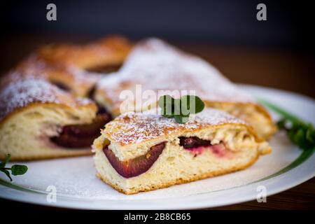 Süß gebackener hausgemachter Pflaumenkuchen mit Puderzucker auf einem Holztisch Stockfoto