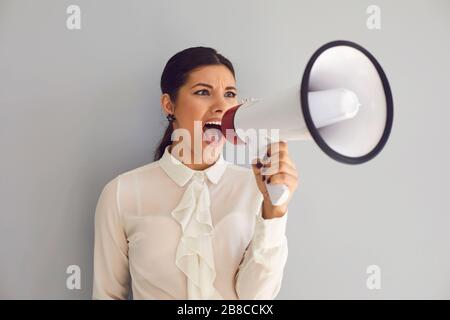 Hispanische Frau mit einem Lautsprecher in ihren Händen, die schreit, kündigt den Nachrichtenprotest auf grauem Hintergrund an. Stockfoto