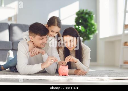 Die glückliche Familie spart Geld in einem Schweineschwein. Sparkonzept für die Geldfinanzierung. Stockfoto