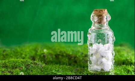 Banner Weiße Tabletten in einer Flasche Wassertropfen auf grünem Hintergrund. Regen. Nutzung, Natürlichkeit, Homöopathie, Natur Stockfoto