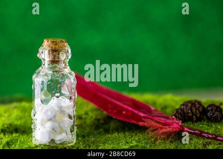 Banner Weiße Tabletten in einer Flasche Wassertropfen und rote Feder auf grünem Hintergrund. Regen. Nutzung, Natürlichkeit, Homöopathie, Natur Stockfoto