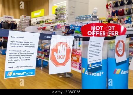 Coronavirus Warnschilder und Sicherheitsbarrieren in einer Amcal Apotheke am internationalen Abflugterminal des Flughafens Sydney (Kingsford Smith) in Australien. Der Chemiker hatte die Barriere und Warnungen am Ladeneingang platziert, um Flugpassagiere, die gerade nach Australien gekommen waren, zu bitten, sich an "soziale Distanzierungsregeln" zu halten, um das Risiko einer Verbreitung des Coronavirus zu verringern. Stockfoto