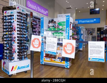 Coronavirus Warnschilder und Sicherheitsbarrieren in einer Amcal Apotheke am internationalen Abflugterminal des Flughafens Sydney (Kingsford Smith) in Australien. Der Chemiker hatte die Barriere und Warnungen am Ladeneingang platziert, um Flugpassagiere, die gerade nach Australien gekommen waren, zu bitten, sich an "soziale Distanzierungsregeln" zu halten, um das Risiko einer Verbreitung des Coronavirus zu verringern. Stockfoto