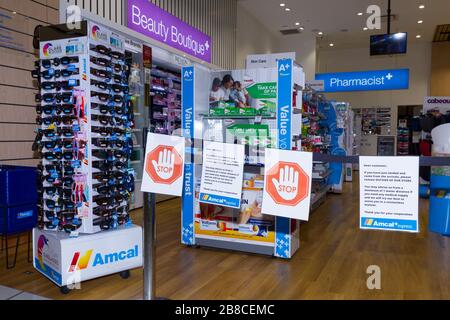 Coronavirus Warnschilder und Sicherheitsbarrieren in einer Amcal Apotheke am internationalen Abflugterminal des Flughafens Sydney (Kingsford Smith) in Australien. Der Chemiker hatte die Barriere und Warnungen am Ladeneingang platziert, um Flugpassagiere, die gerade nach Australien gekommen waren, zu bitten, sich an "soziale Distanzierungsregeln" zu halten, um das Risiko einer Verbreitung des Coronavirus zu verringern. Stockfoto