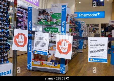 Coronavirus Warnschilder und Sicherheitsbarrieren in einer Amcal Apotheke am internationalen Abflugterminal des Flughafens Sydney (Kingsford Smith) in Australien. Der Chemiker hatte die Barriere und Warnungen am Ladeneingang platziert, um Flugpassagiere, die gerade nach Australien gekommen waren, zu bitten, sich an "soziale Distanzierungsregeln" zu halten, um das Risiko einer Verbreitung des Coronavirus zu verringern. Stockfoto