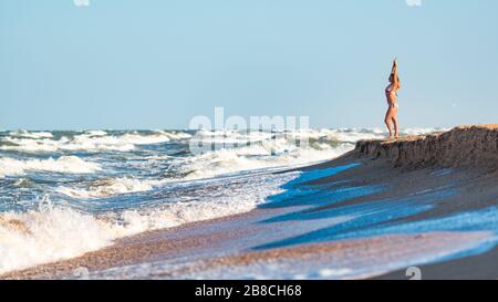 Freudige junge Frau genießt stürmische Meereswellen, die an einem sonnigen Sommertag weit über den Horizont blicken und sich auf dem Meer entspannen. Konzept des Urlaubs Stockfoto