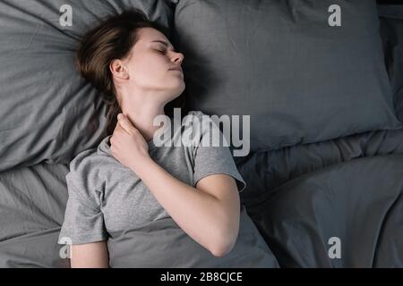 Müde verärgert Frau mit geschlossenen Augen Massage angespannte Nackenmuskeln im Bett liegen, Stressabbau, erschöpfte Mädchen leiden an Schmerzen, Physik Beschwerden Stockfoto