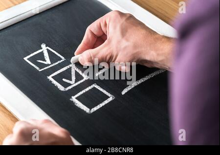 Mann, der ein Häkchen in die Checkliste auf der Tafel schreibt. Dokumentation der fertigen Arbeit und der abgeschlossenen Aufgaben auf dem Schwarzen Brett. Liste auf Planung prüfen. Stockfoto