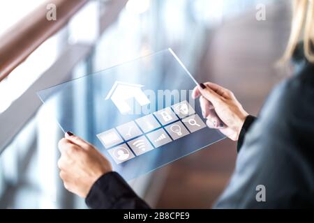 Futuristische, intelligente Heimsteuerung mit transparentem Tablet. Person, die ein digitales automatisiertes System verwendet. Mobiles Glasgerät im modernen Haus. Stockfoto