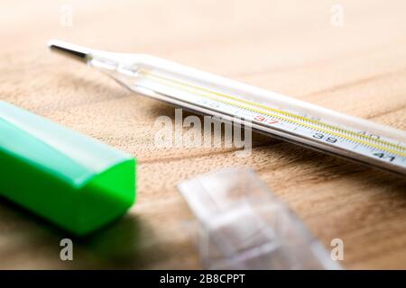 Thermometer auf Holztisch mit Paket. Körpertemperaturmessung im Gesundheitswesen und im medizinischen Bereich. Fieber, Grippe, Krankheit, Virus. Stockfoto