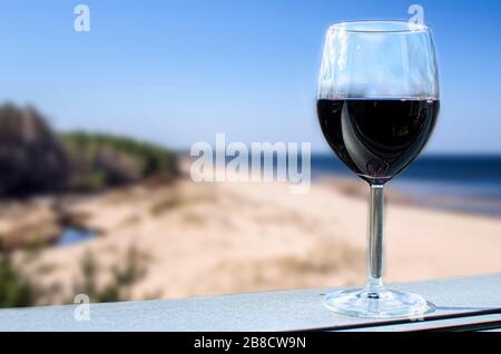 Glas Rotwein mit blauem Meer und Strand Hintergrund. Ostsee Landschaft in Lettland Stockfoto