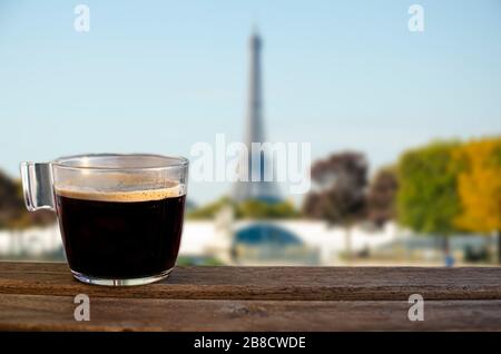 Tasse schwarzen Kaffees auf Holztisch mit Blick auf den Eiffelturm in Paris, Frankreich Stockfoto