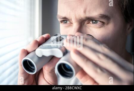 Mann mit Fernglas. Privatdetektiv, Agent oder Ermittler, der das Fenster betrachtet. Mann ausspioniert oder untersucht. Privatsphäre, Überwachung oder Spionage. Stockfoto