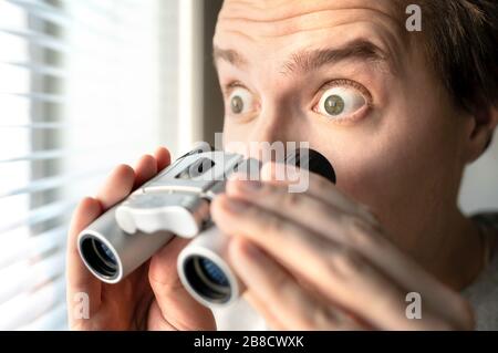 Überraschter Mann mit Fernglas. Neugieriger Kerl mit großen Augen. Neugieriger Nachbar, der Geheimnisse, Tratsch und Gerücht anplauscht oder schnupft. Albern lustiges Gesicht. Stockfoto