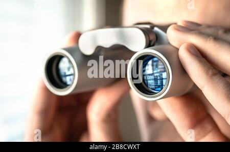 Mann, der mit einem Fernglas aus dem Fenster schaut. Neugieriger und neugieriger Nachbar. Privatdetektiv oder Undercover-Cop-Untersuchung oder Spionage. Neugierige Person. Stockfoto