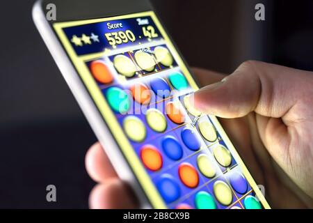 Mobiles Spiel auf dem Smartphone-Bildschirm. Junger Mann spielt Puzzle-Spiel in der Telefon-App. Gamer haben Spaß. Digitales Gaming-, Entertainment- und Videospielkonzept. Stockfoto