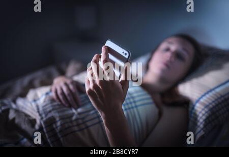 Traurige Frau, die nachts im Bett auf das Smartphone blickt. Anruf von unbekanntem Anrufer. Schlaflose Person, die unter Stress oder Schlaflosigkeit leidet. Stockfoto