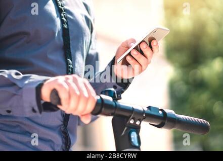 Elektrokick Roller Verleih App im Telefon. Mann, der ein E-Fahrzeug zum Pendeln mit dem Smartphone mietet. Mobile Anwendung für den Ökostrom. Stockfoto