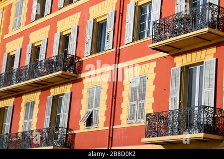 Typisch orangefarbene Fassade provenzalischer Gebäude mit kleinen Metallbalkons und bunten Fensterläden in Nizza, französische Riviera, Südfrankreich. Stockfoto