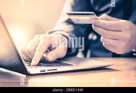 Mann, der mit Kreditkarte und Laptop online bezahlt. Digitaler E-Commerce-Service. Zufriedene Kunden kaufen und bezahlen im Internet mit Computer. Stockfoto