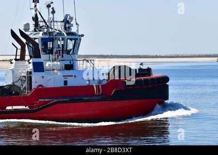 Vor dem Strand liegt eine Schleife in der Nähe des modernen, leuchtend roten Schleppboots im Rotterdamer Hafen Stockfoto