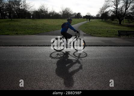 Ein Mann auf einem Fahrrad, der durch den Greenwich Park in London fährt, nachdem Premierminister Boris Johnson Pubs, Cafés, Nachtclubs, Bars, Restaurants, Theater, Freizeitzentren und Fitnessstudios bestellt hatte, um Coronavirus zu bekämpfen. Stockfoto