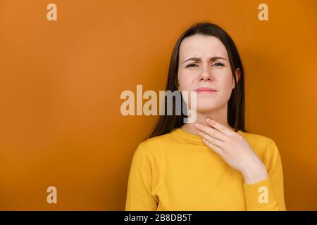 Unzufrieden junge Frau hat Halsschmerzen, krank und unwohl, Stirnrunzeln Gesicht, fühlt Schmerzen nach Erkältung, trägt gelben Pullover Stockfoto