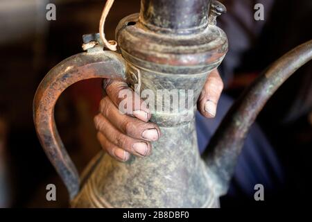 Lokaler Handwerker, der in seiner Werkstatt in Chiwa, Usbekistan, ein altes Metallglas zum Kochen von Tee hält Stockfoto